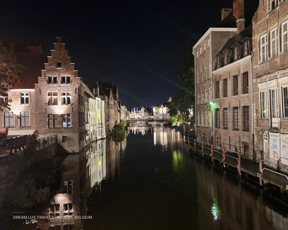 Illuminated historic buildings reflected in a canal in Ghent at night.