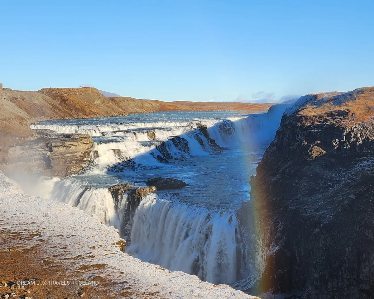 Gullfoss waterfall flowing through a sunlit landscape in Iceland.